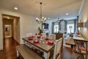A dining area with a wooden table set for four, white chairs, and a chandelier. - Welcome to Rising Tide! (Tuscaloosa)