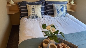 Cama bem arrumada com almofadas listradas, mesa de cabeceira com abajur e bandeja com doces e uma flor.