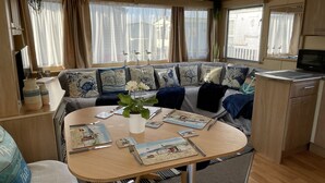 Interior acolhedor de uma RV, com área de refeições, cozinha e espaço de estar com vista para o exterior.
