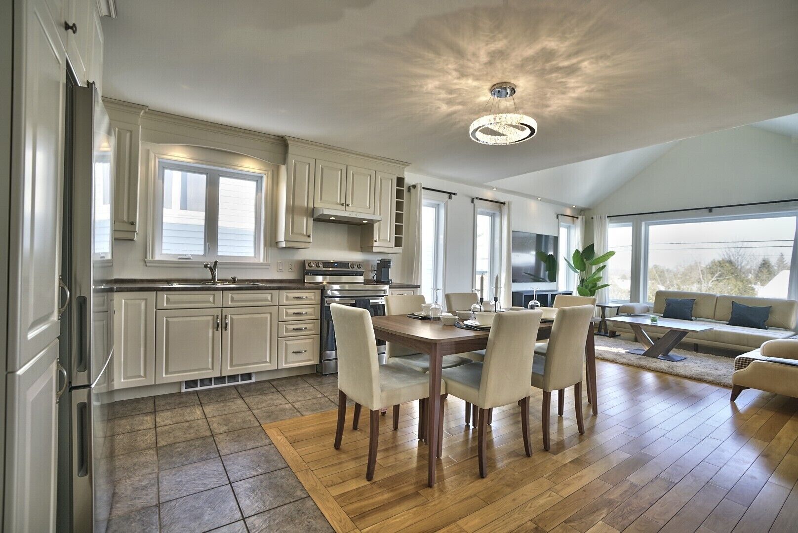 A spacious kitchen with modern appliances, a dining area with a wooden table and chairs, and a cozy seating area with a sofa and a plant.