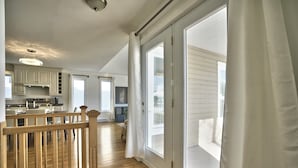 Ein großzügiger Wohnbereich mit einer Holztreppe, einer Küche mit weißen Schränken und großen Schiebegläsern, die auf einen Balkon führen.