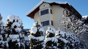 Un edificio de varios pisos con techo inclinado, ventanas grandes y árboles cubiertos de nieve al frente.