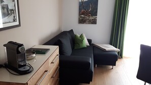 A modern living room with a sofa, a small table with a coffee machine, and a framed picture on the wall.