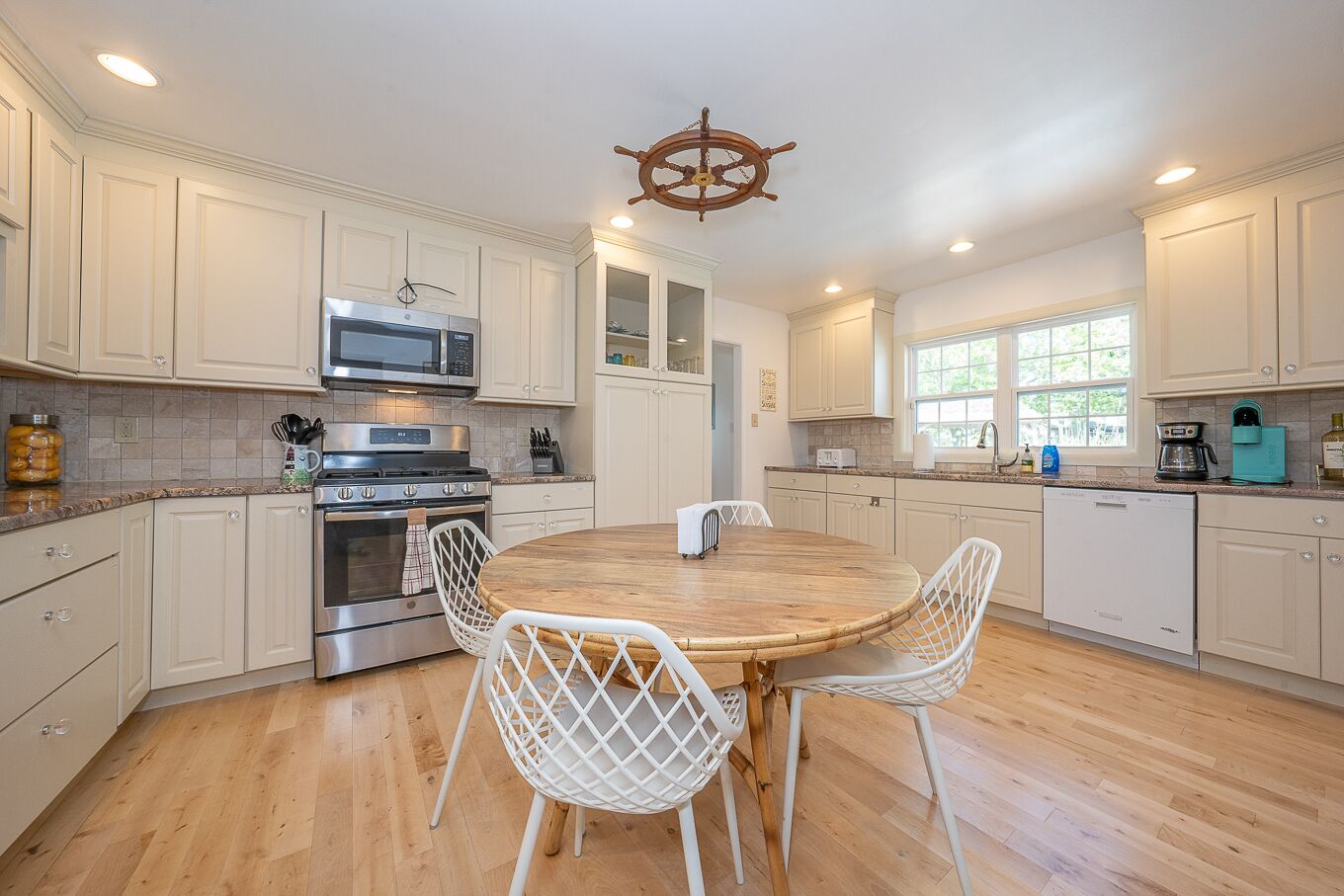 A modern kitchen with white cabinetry, a central island with chairs, a microwave, stove, and a coffee maker.