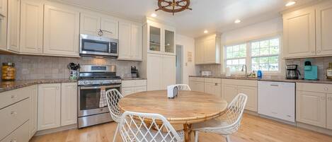 A modern kitchen with white cabinetry, a central island with chairs, a microwave, stove, and a coffee maker.
