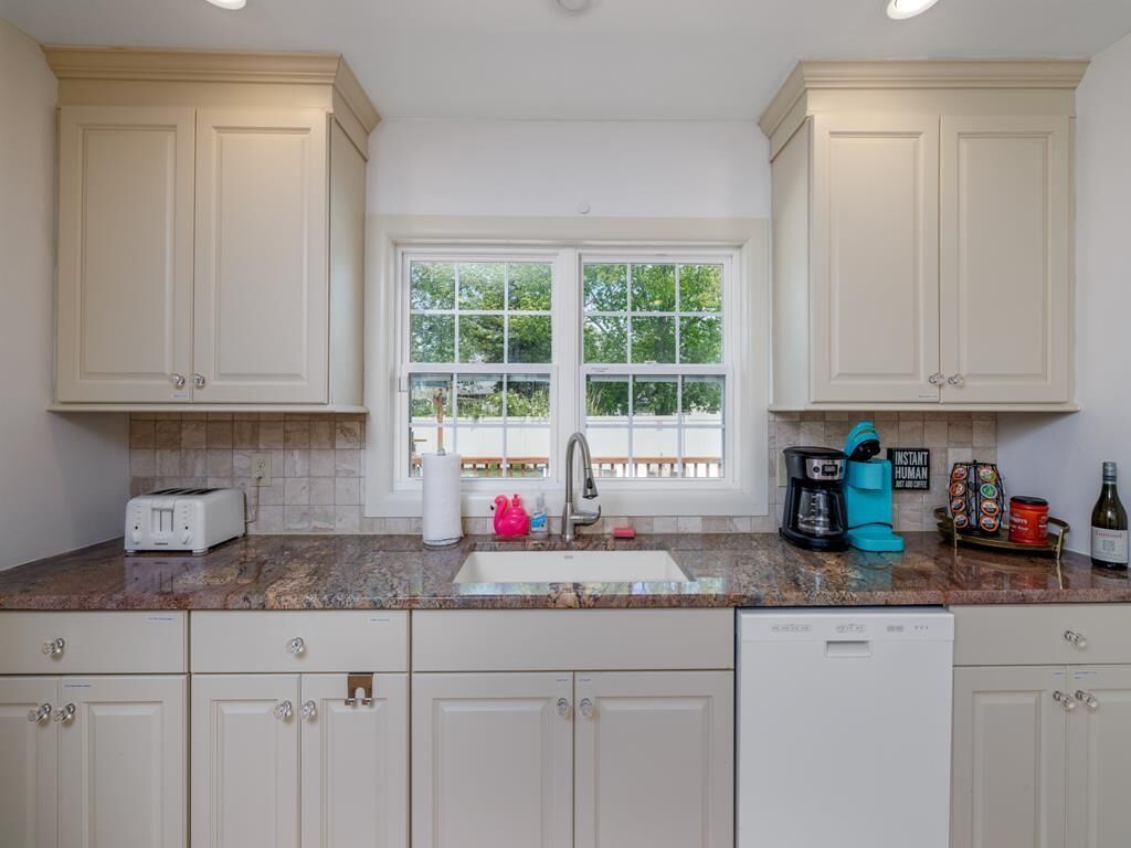 A kitchen with white cabinets, a granite countertop, a double sink, a toaster, a coffee maker, and a dishwasher.