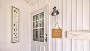 Una puerta blanca con un cartel que dice 'BIENVENIDOS', un buzón y un letrero colgante que dice 'Bienvenidos, quítense los zapatos y pasen'.