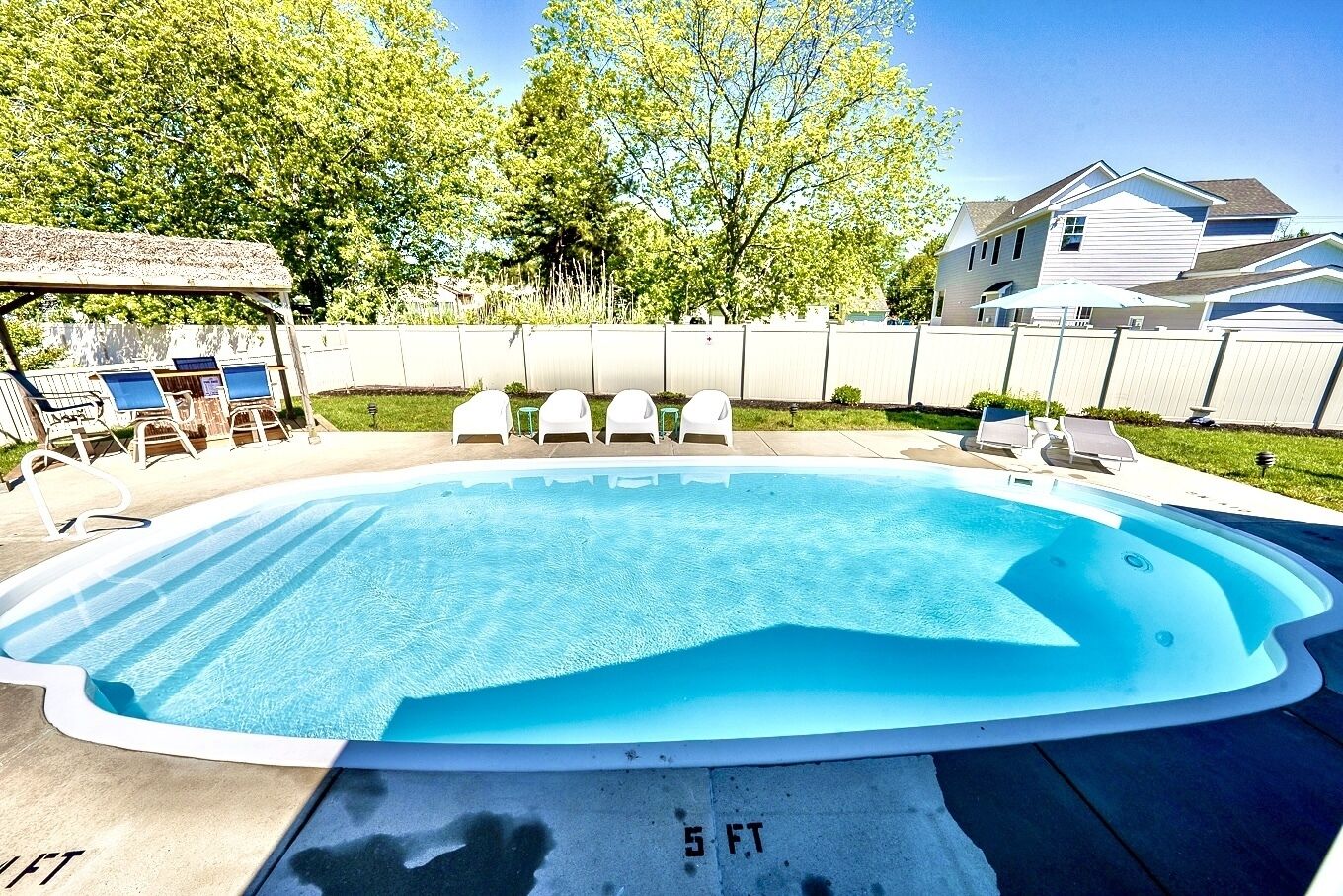 Piscina rectangular con indicador de profundidad de 1.5 metros, rodeada por una cerca blanca y protegida por árboles.