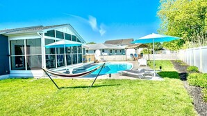 Un patio trasero con piscina, una hamaca y un porche cubierto.