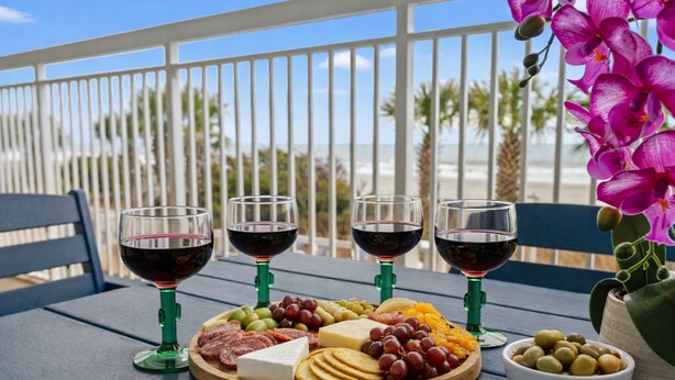 A table with a charcuterie board, three glasses of red wine, and a potted orchid.