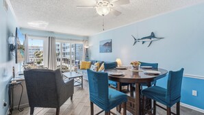 Een eetruimte met een ronde tafel, blauwgroene stoelen en een plafondventilator.