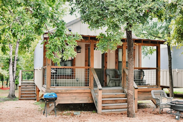 A wooden deck with a chair, a barbecue grill, and a covered seating area. - 2 Son's Geronimo - Birdhouse Cabin (Seguin)