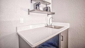A kitchen with a white countertop, stainless steel sink, and two wall-mounted shelves above the sink. - Studio 6 Effingham, Il (Effingham)