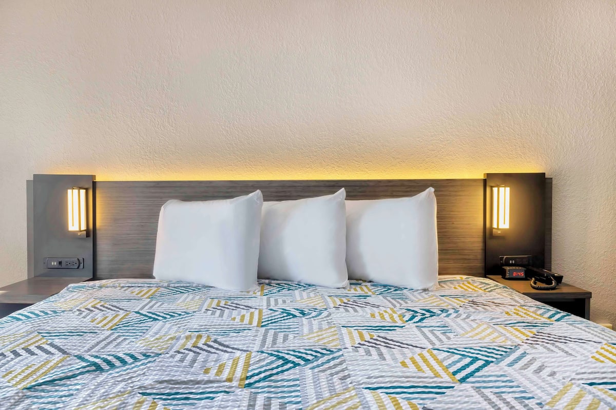 A hotel room with a bed, two bedside tables, and a nightstand with a phone and clock.
