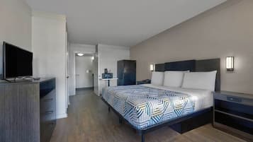 Quarto de hotel moderno com cama, mesa de cabeceira, televisão e uma pequena cozinha.