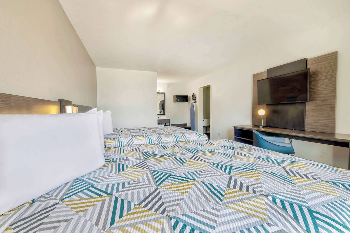 A hotel room with two beds, a desk with a flat-screen TV, and a mirror.