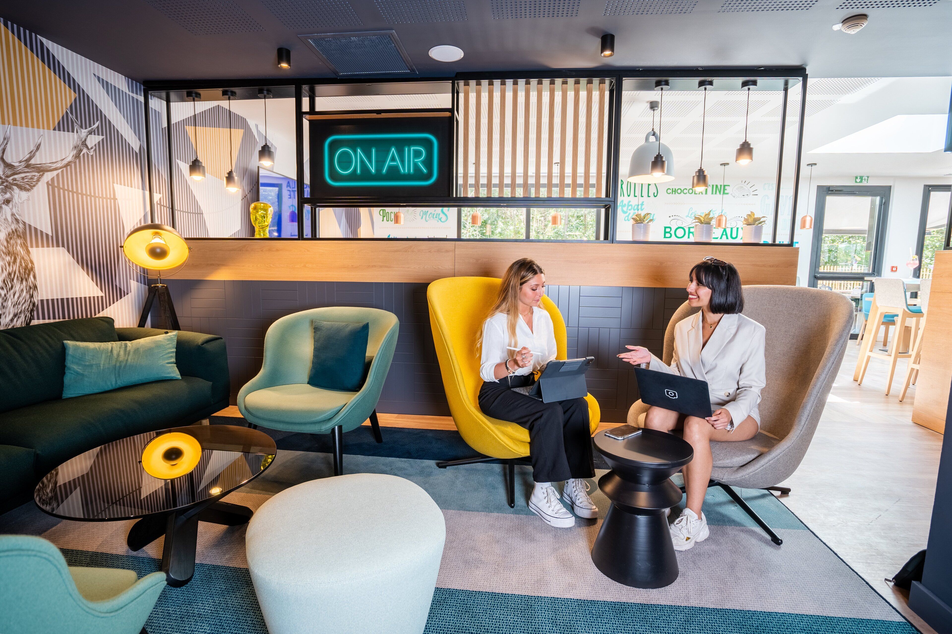 A modern lounge area with a neon 'ON AIR' sign, comfortable seating, and a wooden counter with 'Boreau' branding.