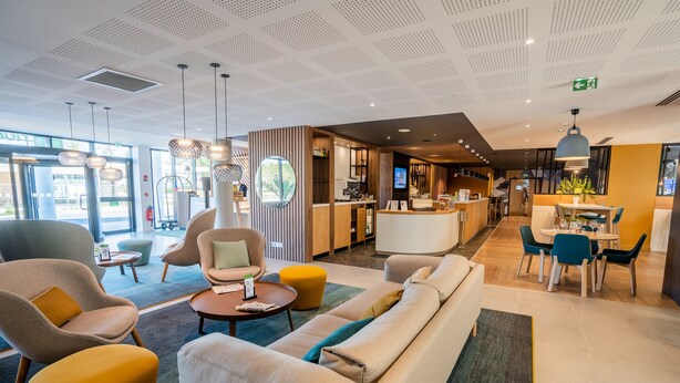 A modern hotel lobby with seating areas, a reception desk, and a dining area. - Holiday Inn Bordeaux-Merignac by IHG (Merignac)