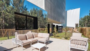 An outdoor seating area with a beige sectional sofa, white metal chairs, and a small white table. - Holiday Inn Bordeaux-Merignac by IHG (Merignac)