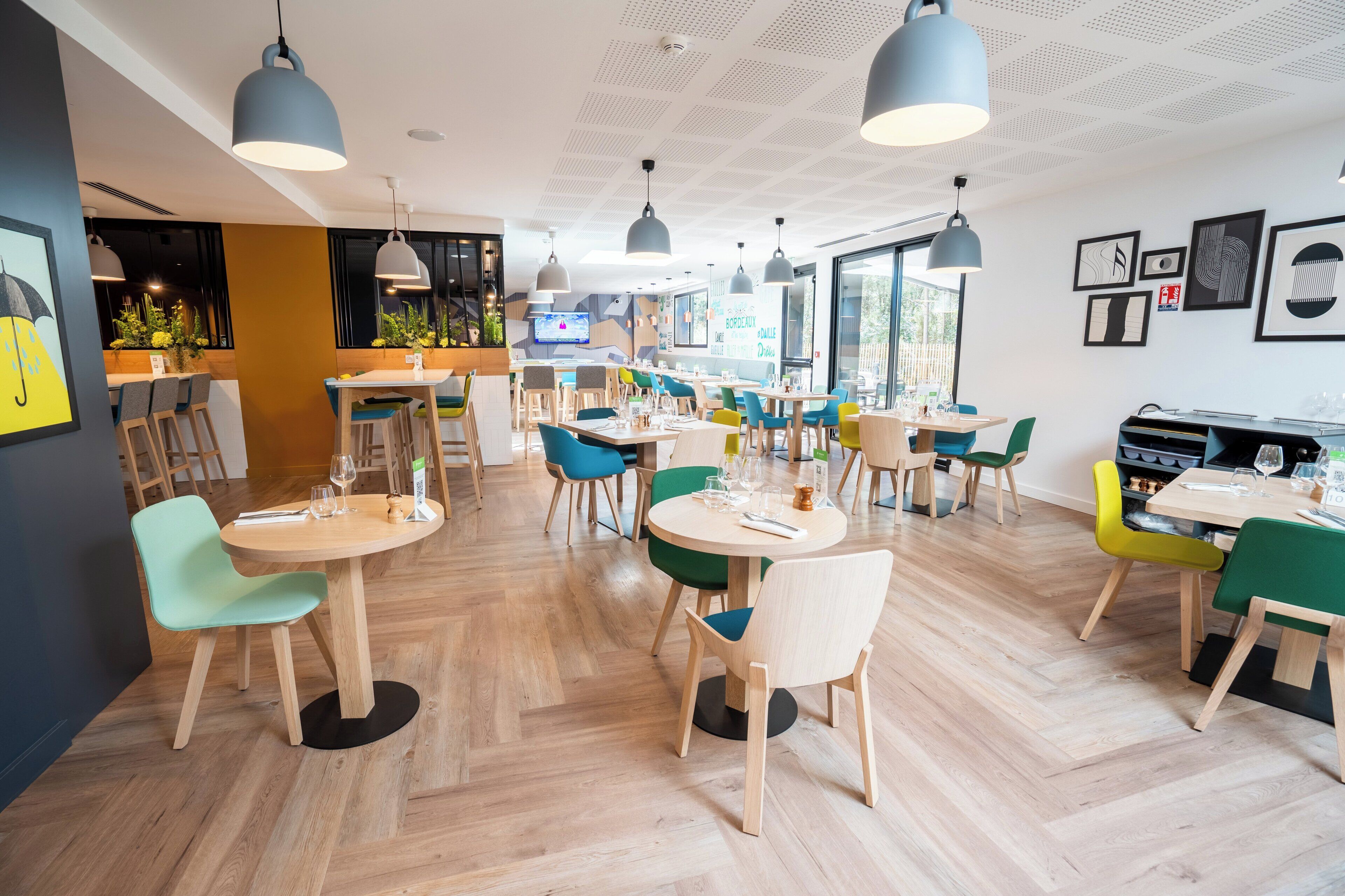 A modern restaurant interior with round tables, colorful chairs, and pendant lighting.