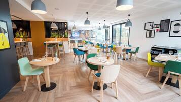 A modern restaurant interior with round tables, colorful chairs, and pendant lighting.
