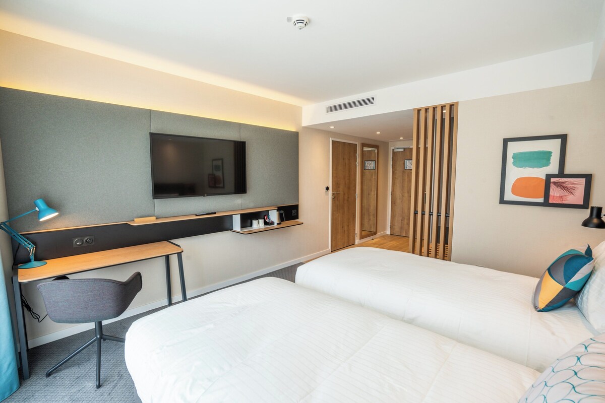 A hotel room with a bed, a desk, a chair, a television, and a wardrobe.