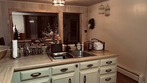Une cuisine avec un plan de travail en bois, un évier et un panneau sur lequel on peut lire : « J’aime les câlins et les baisers, mais ce que je préférerais, c’est un coup de main pour faire la vaisselle. »
