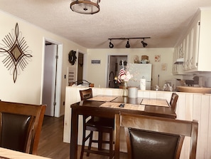 Un comedor con una mesa y sillas de madera, un candelabro y una cocina al fondo.