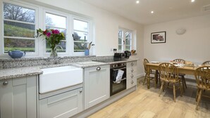 Eine Küche mit weißen Schränken, einer Arbeitsplatte aus Granit, einem eingebauten Backofen und einem Essbereich mit Holztischen und einem Tisch.