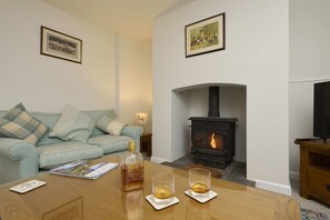 A living room with a sofa, a table with a bottle and glasses, a fireplace, and framed pictures on the wall.