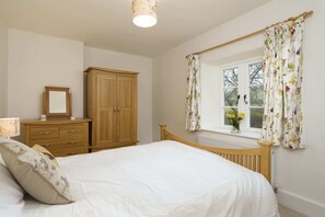 A bedroom with a wooden bed, a nightstand, a wardrobe, and a window with floral curtains.