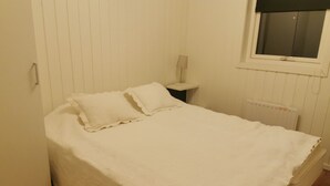 A neatly made bed with a white bedspread and pillows in a room with white walls and a window with a black blind. - Modern guesthouse in the middle of Torhamn (Blekinge län)