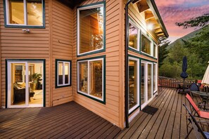 Een houten huis met twee verdiepingen, grote ramen, een terras en tuinmeubilair.