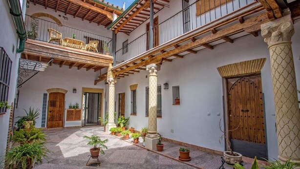 Un patio con una pérgola de madera, plantas en macetas y una puerta de madera.