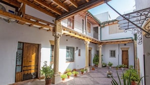 Un patio con una pérgola de madera, plantas en macetas y un pequeño carrito.