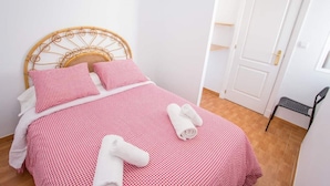 Una cama bien hecha con una colcha a cuadros y almohadas, un cabecero de mimbre y una puerta blanca al fondo.