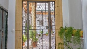 Una entrada porticada con arco decorativo, un farol colgante y plantas en macetas a la derecha.
