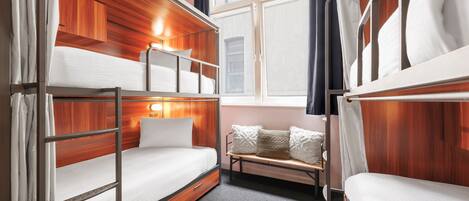 Een slaapkamer met stapelbed, houten lambrisering, een bank met kussens en een raam met gordijnen.