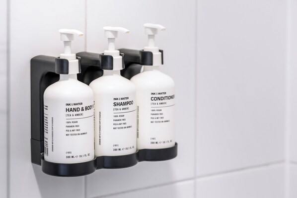 Tres botellas de productos para manos y cuerpo sobre un dispensador negro en un baño.