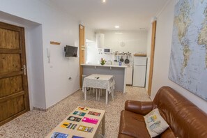 A compact living space with a kitchenette, a small dining table, a brown leather sofa, and a coffee table with magazines.