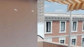 A balcony with a wooden table and chairs, a striped awning, and a view of a brick building with windows. - Private penthouse with terrace in the historic center (Jerez de la Frontera)