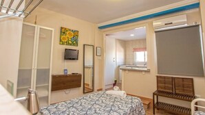 A bedroom with a bed, a TV, a mirror, a bench, and a bathroom visible through an open door. - Private penthouse with terrace in the historic center (Jerez de la Frontera)