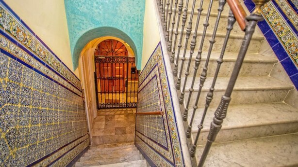 A staircase with ornate blue and yellow tiles on the walls and a metal railing. - Private penthouse with terrace in the historic center (Jerez de la Frontera)