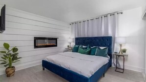 A modern bedroom with a blue bed, white walls, a mounted fireplace, and a small side table with a lamp. - The Beach Bungalow - In the Heart of Destin, FL!   (Destin)