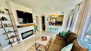A modern living room with a sofa, coffee table, and shelves. A kitchen is visible in the background. - The Beach Bungalow - In the Heart of Destin, FL!   (Destin)