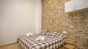 Un dormitorio con pared de piedra, cama con ropa de cama a cuadros y una mesita de noche de madera.
