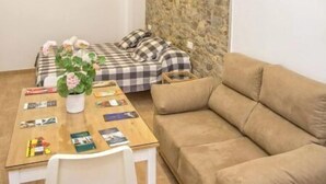 Una habitación acogedora con una mesa de madera, un sofá color beige, una cama con ropa de cama a cuadros y una pared de acento de piedra.