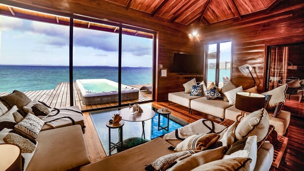 A wooden interior with a large window overlooking the sea, a hot tub, and a cozy seating area.