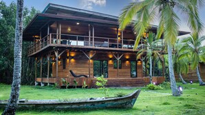 A wooden building with a balcony, surrounded by palm trees and a boat in the foreground.