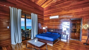 A wooden room with a bed, a table, and a view of the ocean.